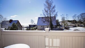 Lumipeitteinen terassi, jossa on valkoinen kaide, pyöreä pöytä ja näkymä taustalla oleviin taloihin ja puihin.