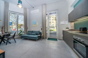 A modern apartment with a sofa, dining table, chairs, kitchenette, and large windows.