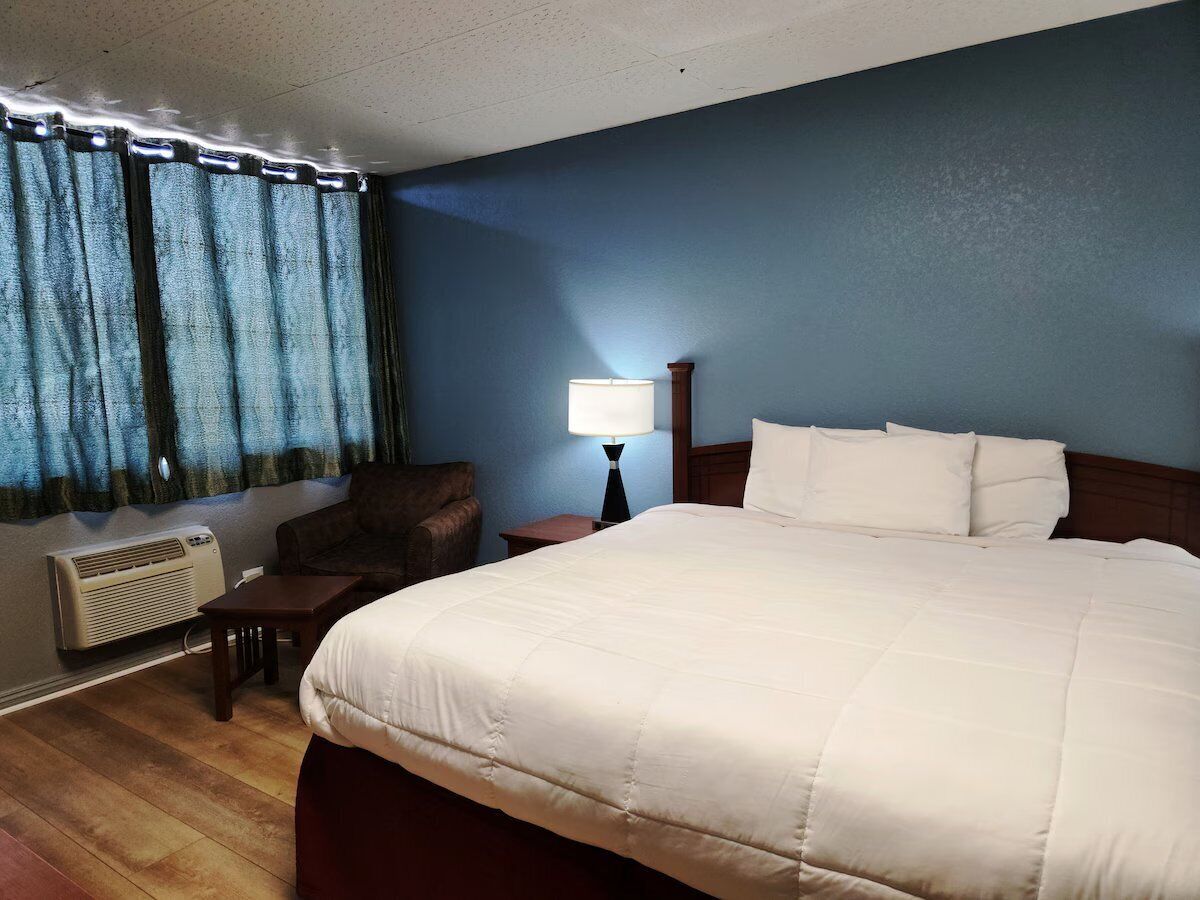 A hotel room with a large bed, a chair, a nightstand with a lamp, and a window with curtains.