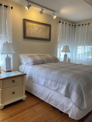 A neatly made bed with a quilt, two bedside lamps, a nightstand with a lamp, and a framed picture on the wall.