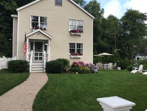 A two-story house with a front porch, a welcome sign, and a flag.