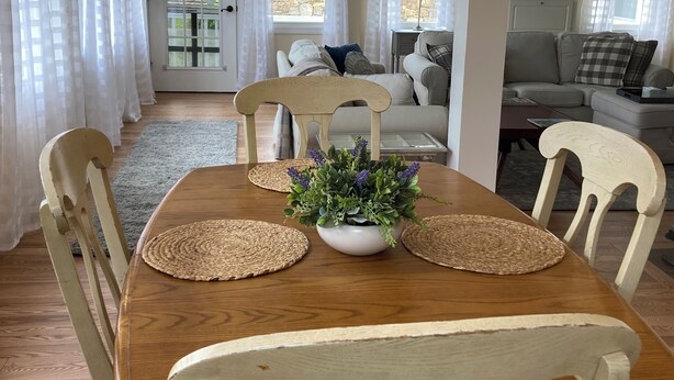 A dining area with a wooden table, white chairs, a chandelier, and a potted plant.