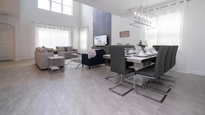 Ein modernes Wohnzimmer mit Essbereich, ausgestattet mit einem großen Fernseher, grauen Sofas und einer Deckenleuchte.