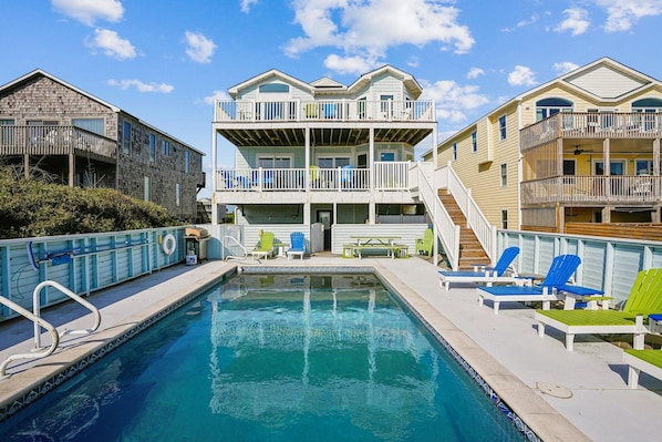Guests can enjoy a balcony with a view of the pool area, surrounded by lounge chairs and a table.