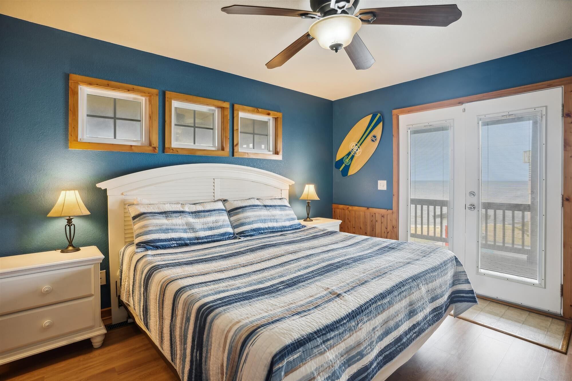 A bedroom with a bed, two bedside tables, a ceiling fan, and a door leading to a balcony.