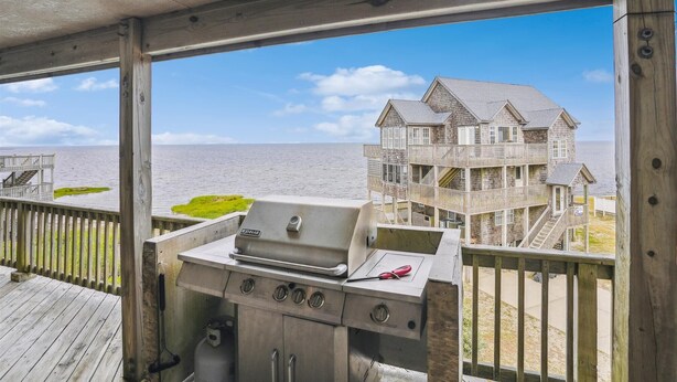 A wooden deck with a grill and a view of a beach house. - 7130- Sunset Breeze - Soundfront Waves | Pool & Sunset Views (Waves)