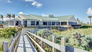 A coastal building with a wooden deck leading to a gated entrance, surrounded by vegetation. - OV 914 Partial Course View Condo - Paradise Rental in Ocean Village (Fort Pierce)