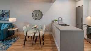 A modern kitchen with a central island, a dining area with a glass table and chairs, a sofa with a blue throw pillow, and a round mirror on the wall. - 645 Fresh Modern Condo Inside Resort Gates - Free Wifi - Walk to Spa (Carlsbad)