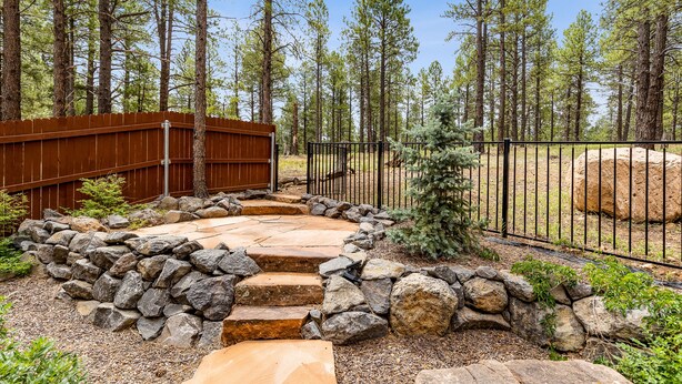 A stone pathway leading to a wooden bridge, surrounded by a metal fence and a forested area. - Pinnacle Pines | Forest Views | Modern Home with EV Charger | Direct Trail Access (Flagstaff)