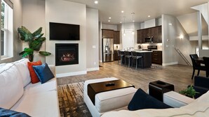 A modern living room with a fireplace, a dining area, and a kitchen with a bar. - Pinnacle Pines | Forest Views | Modern Home with EV Charger | Direct Trail Access (Flagstaff)