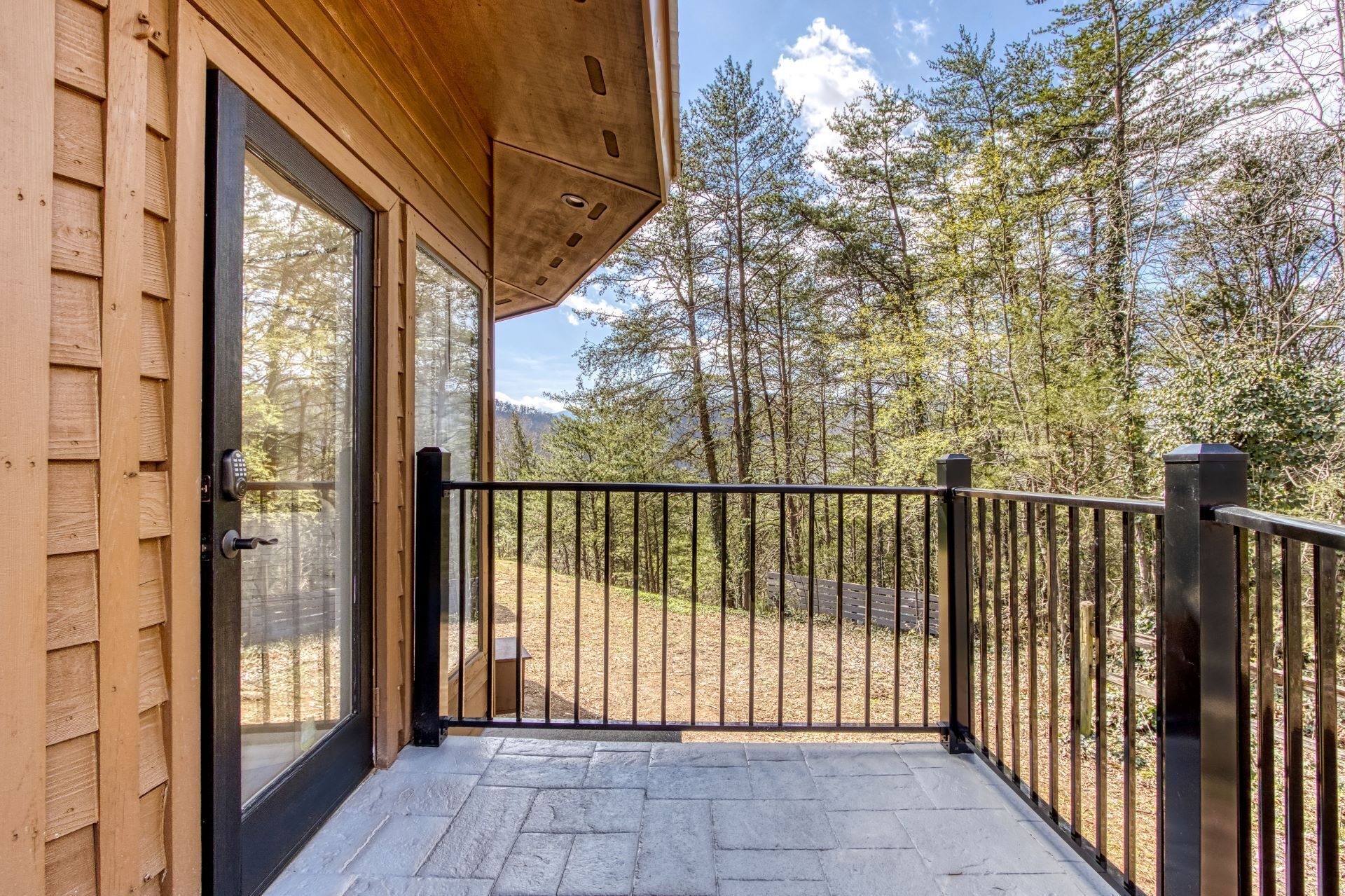 Una baita di legno con una porta vetrata che si apre su un portico con pavimento in pietra.