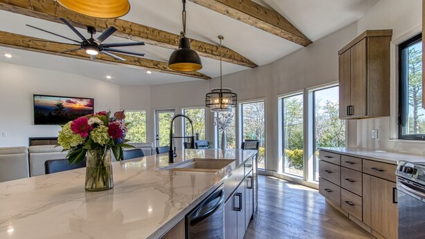 A modern kitchen with a large island, wooden beams, and large windows. - Mountain Valley Revival - Brand New Renovations, Close To Town, Panoramic Mountain Views! (Pigeon Forge)