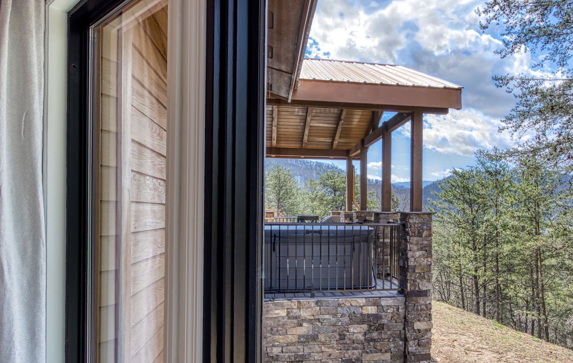 A covered outdoor area with stone walls, a metal railing, and a view of a forested landscape.