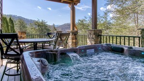 A hot tub with a stone wall and a wooden deck, overlooking a mountainous landscape. - Mountain Valley Revival - Brand New Renovations, Close To Town, Panoramic Mountain Views! (Pigeon Forge)