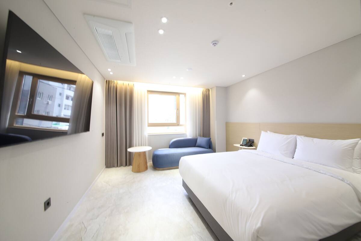 Ein modernes Hotelzimmer mit einem großen Bett, einer Sitzecke, einem kleinen runden Tisch und einem an der Wand befestigten Fernseher.