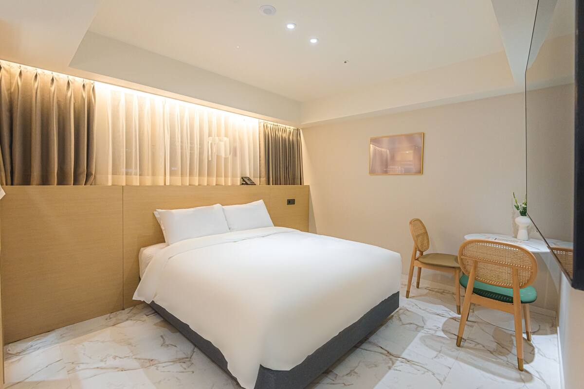 Ein Hotelzimmer mit einem großen Bett, einem Schreibtisch mit Stuhl und einem Fenster mit Vorhängen.