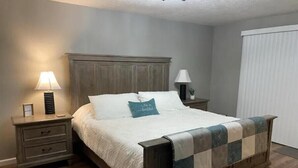 Une chambre à coucher avec un lit en bois, deux tables de chevet avec des lampes, une petite table de nuit avec un tiroir et une fenêtre avec des stores.