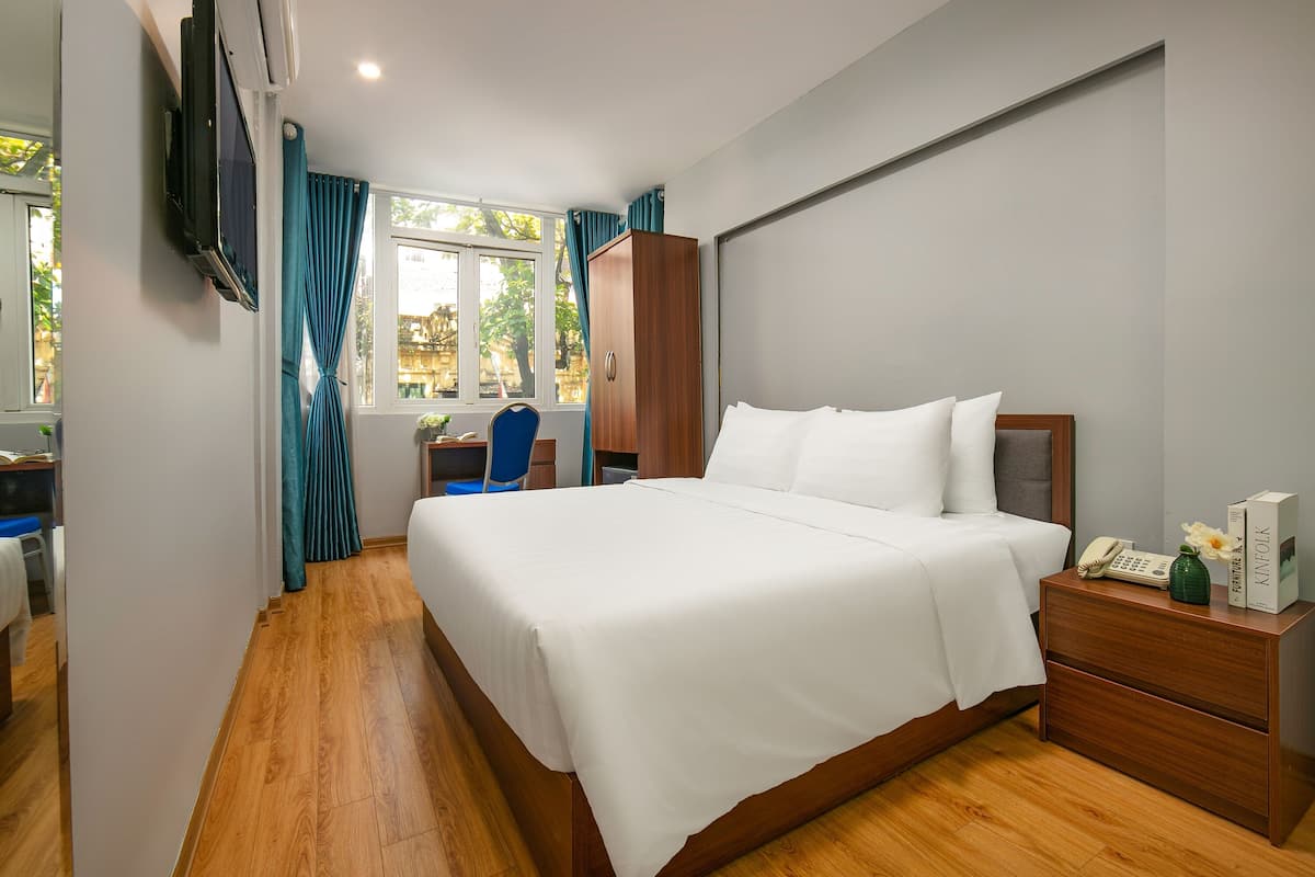 A hotel room with a large bed, a desk with a chair, a wardrobe, and a window with curtains.