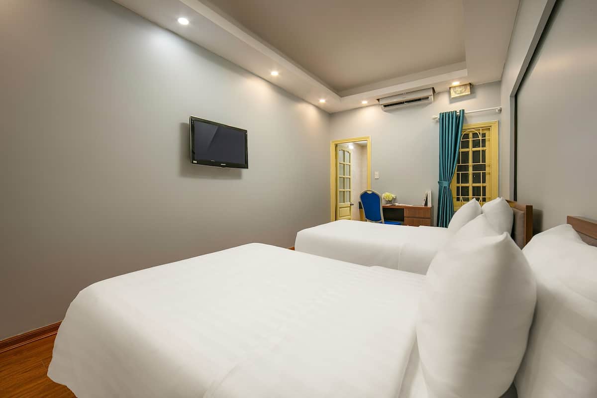 A hotel room with two beds, a television, a desk, and a window with curtains.