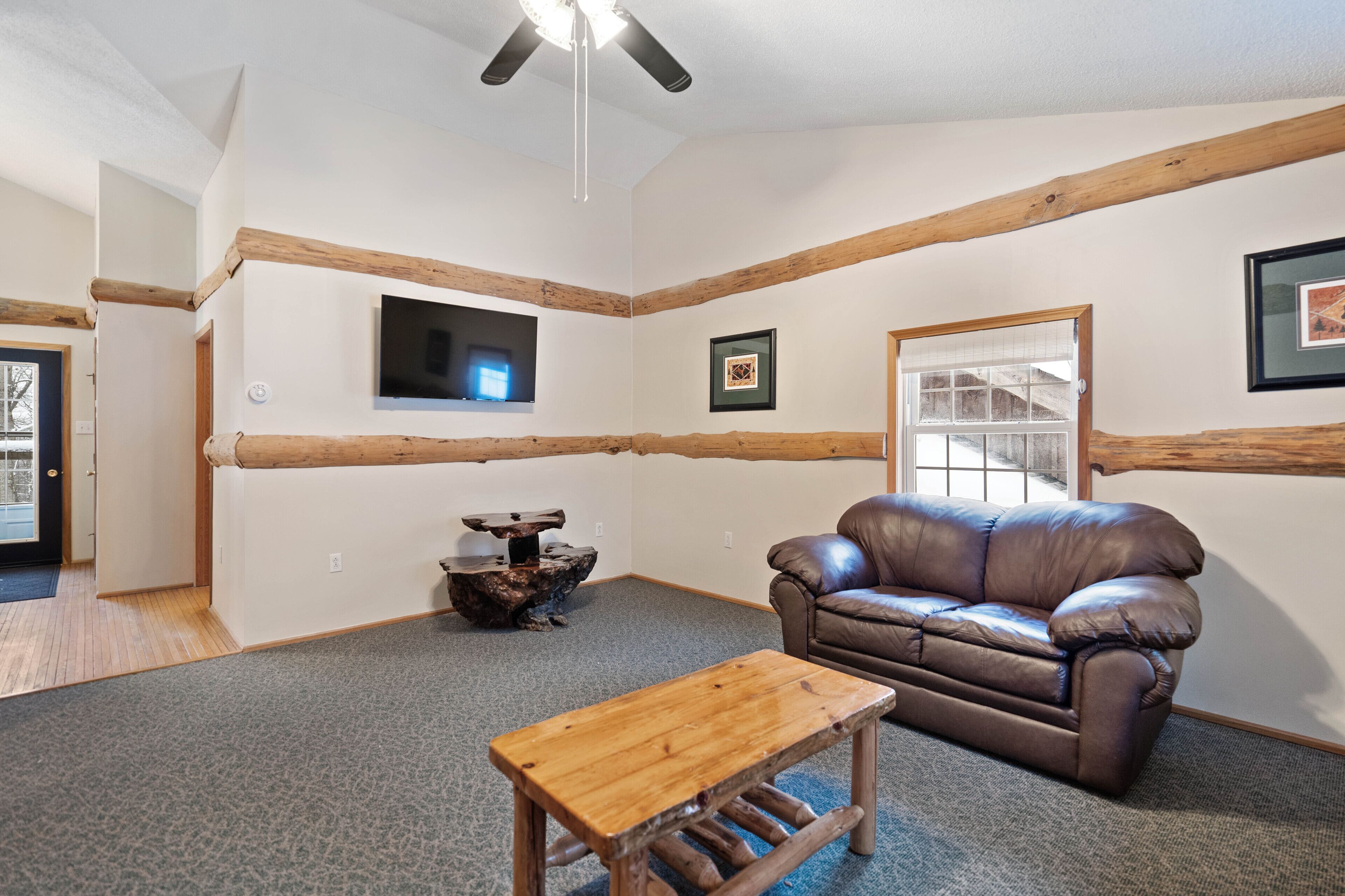 A cozy living room with a brown leather sofa, a wooden coffee table, and a ceiling fan.