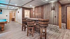 Un coin bar rustique avec des tonneaux et des tabourets en bois, une table de billard et un mur en pierre.