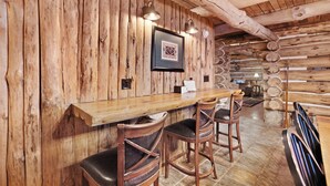 Un coin bar rustique en bois, avec un comptoir en bois, des tabourets de bar et des œuvres d’art encadrées accrochées au mur.