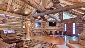 L’intérieur d’une cabane en rondins, avec une cheminée, des meubles en cuir et une tête de cerf fixée au mur.