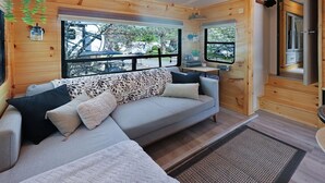 Interior acollidor d'una cabana amb un sofà, una taula petita i una finestra que ofereix vistes cap a l'exterior.