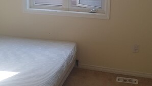 A bedroom with a single bed, a window, and a carpeted floor.