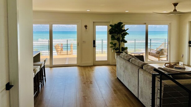A spacious living area with a large sliding glass door leading to a balcony with a view of the ocean.