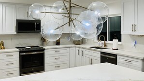 A modern kitchen with white cabinets, a black oven, a stainless steel microwave, and a unique spherical light fixture.