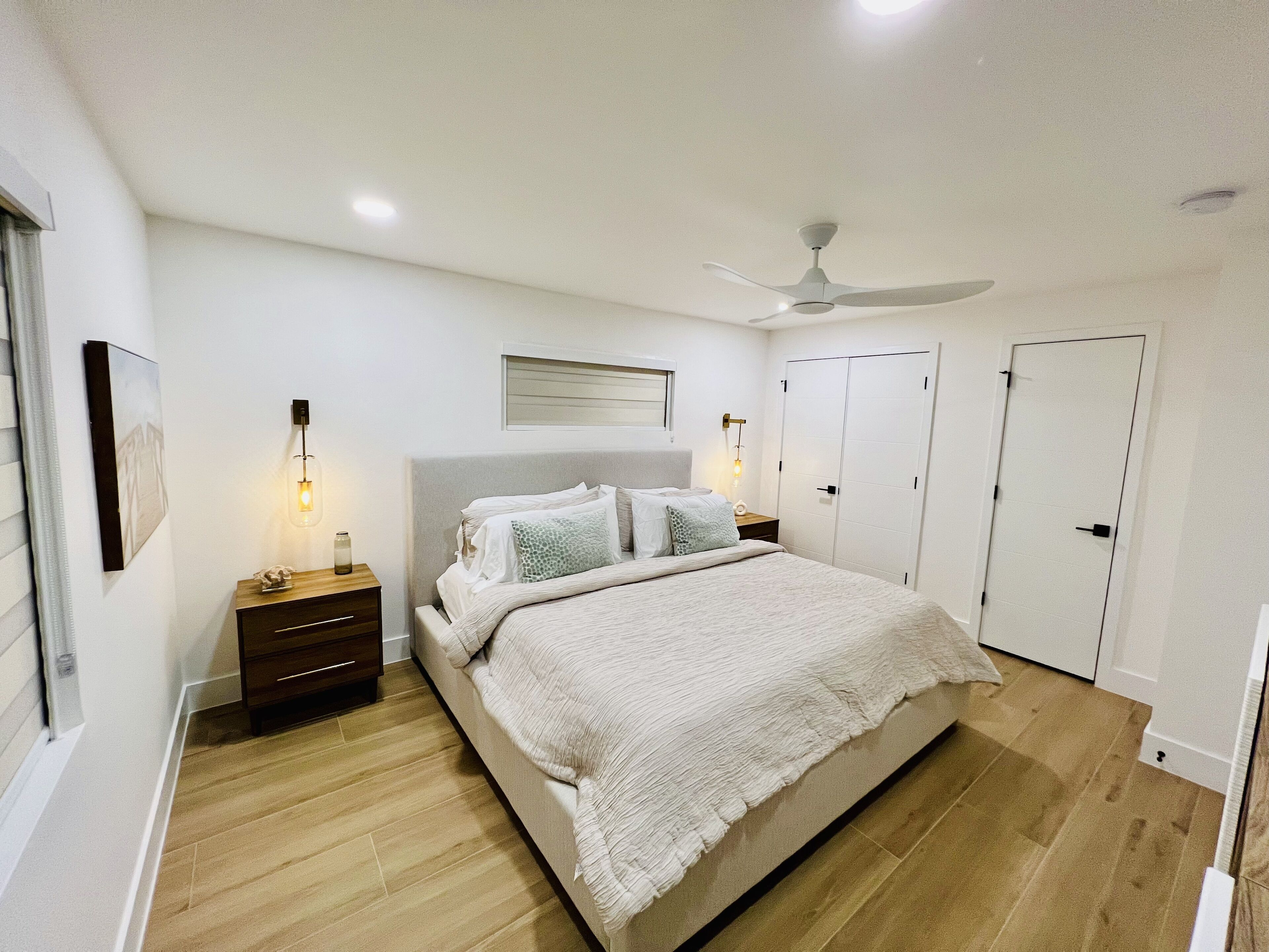 Een slaapkamer met een bed, nachtkastjes, een plafondventilator en een kledingkast.