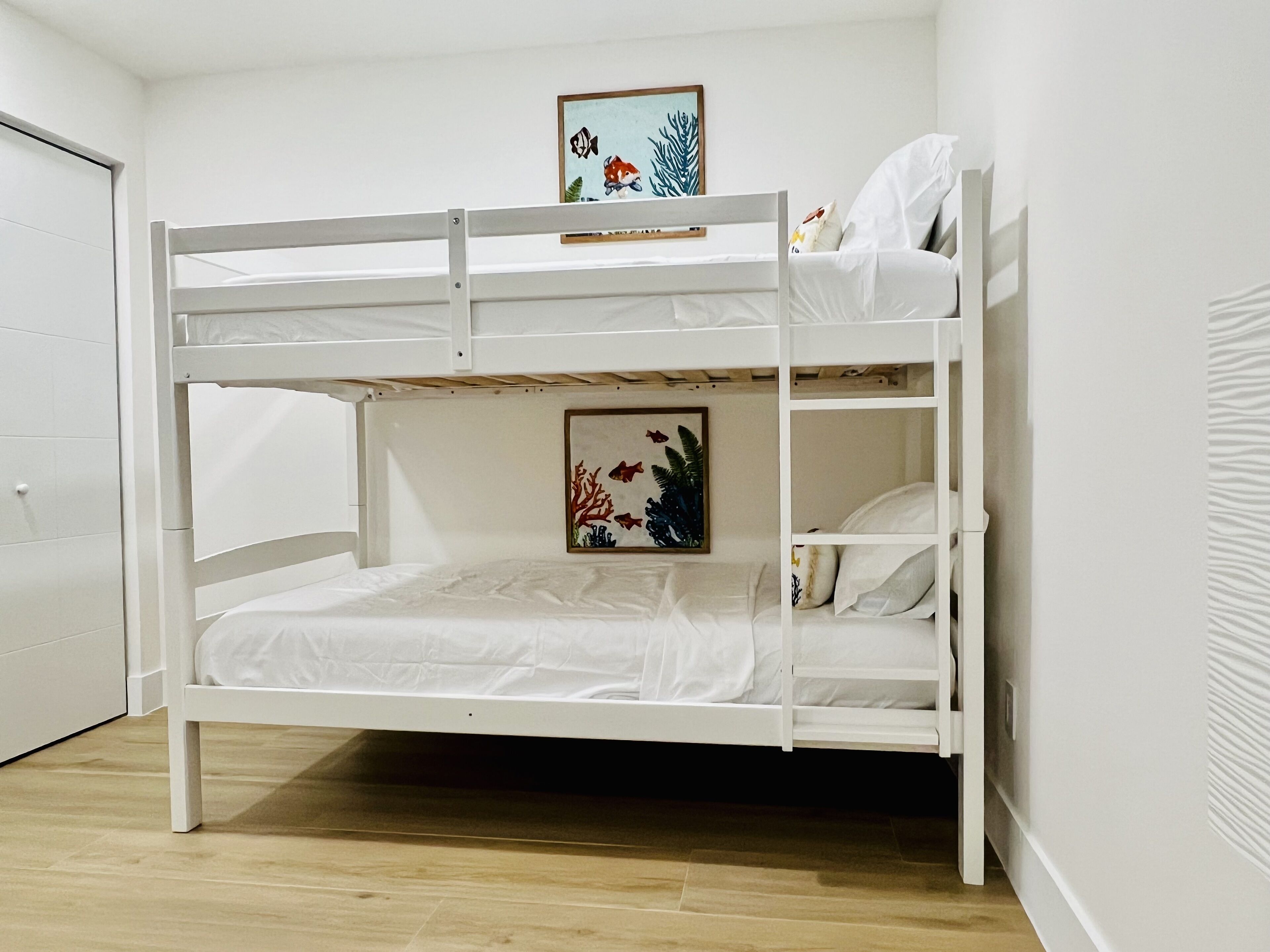 A bunk bed with a lower bunk and a top bunk, white bedding, and a framed picture of fish on the wall above the top bunk.