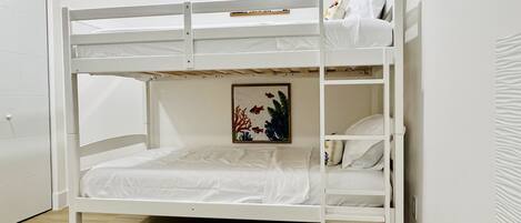 A bunk bed with a lower bunk and a top bunk, white bedding, and a framed picture of fish on the wall above the top bunk.