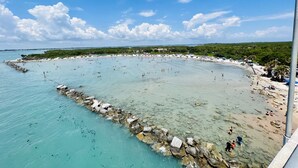 A beach with clear turquoise water, rocky shoreline, and a sandy area with umbrellas and people.