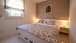 A bedroom with a bed, bedside tables, a window with blinds, and a painting on the wall. - Apartment Diva near the beach (Njivice)