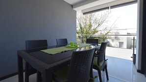 A dining area with a table and chairs, a green placemat, and a window with a view of trees and buildings. - Apartment Diva near the beach (Njivice)