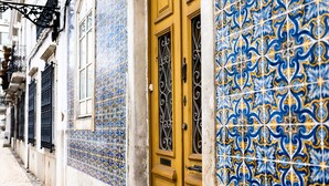 A narrow street with buildings featuring blue and yellow patterned tiles, a yellow door with a metal gate, and a cobblestone pavement. - 5 Star Villa Cyclamen – Luxury Pools & Spa (Algarve)