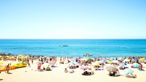 A crowded beach with people sunbathing and swimming, and a boat in the water. - 5 Star Villa Cyclamen – Luxury Pools & Spa (Algarve)