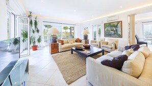 A spacious living room with a large sofa set, a coffee table, and two lamps. There are potted plants and a painting on the walls. - 5 Star Villa Cyclamen – Luxury Pools & Spa (Algarve)