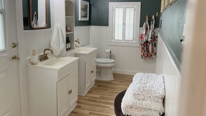 A bathroom with a white vanity, a toilet, a sink, and a mirror. There is a window with blinds and a towel rack with towels. - Spacious guesthouse located in the heart of Weatherford. (Weatherford)