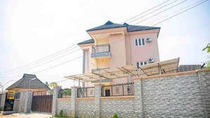A two-story house with a balcony, a gated entrance, and a stone wall. - Cogent Apartments (Uyo)
