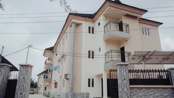 A multi-story residential building with balconies, a gated entrance, and a paved driveway.