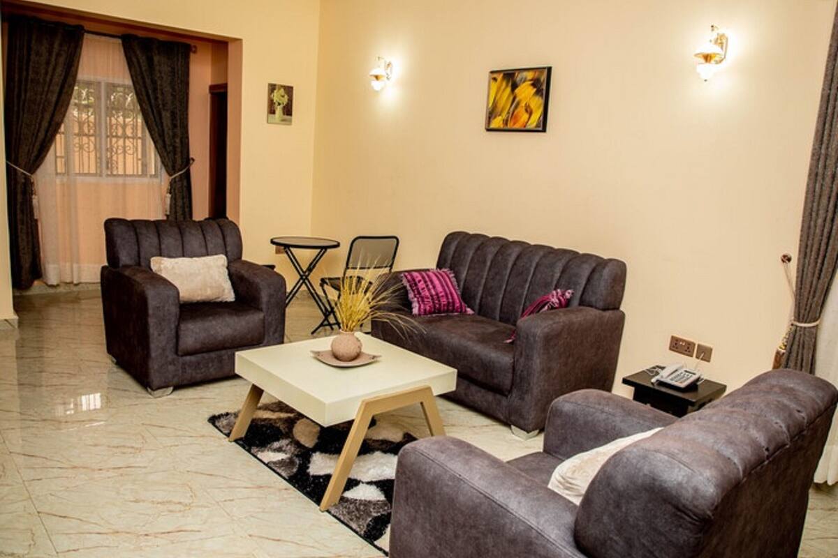 A living room with two sofas, a coffee table, and a small table with a vase. There are two wall-mounted lights and a painting on the wall.