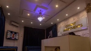A reception area with a chandelier, a TV on the wall, and a sign reading "Cogent Apartments". - Cogent Apartments (Uyo)