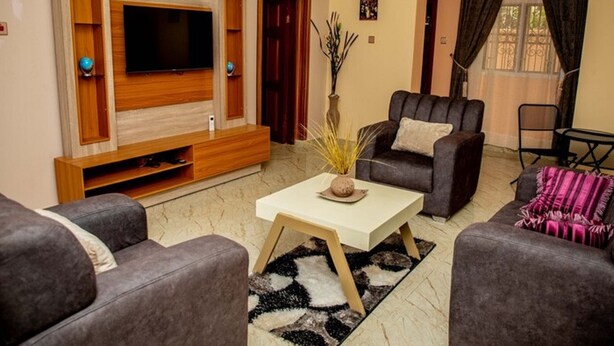 A living room with a flat-screen TV, two sofas, a coffee table, and a decorative vase. - Cogent Apartments (Uyo)