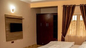 A bedroom with a bed, a wardrobe, a television mounted on the wall, and a window with curtains. - Cogent Apartments (Uyo)