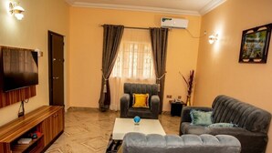 A living room with a flat-screen TV, grey sofas, a coffee table, and a wooden entertainment unit. - Cogent Apartments (Uyo)