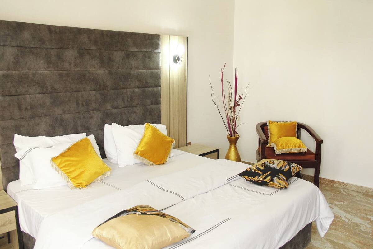 A neatly made bed with white and gold bedding, a wooden headboard, and a bedside table with a lamp.