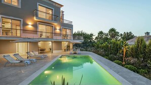 Una casa moderna de dos pisos con piscina, mobiliario de exterior y un jardín bien cuidado.
